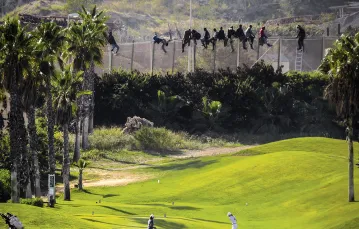 Migranci usiłują przejść przez zabezpieczenia na granicy Maroka z Melillą,  eksklawą Hiszpanii; po stronie „unijnej” – pole golfowe, 2014 r. / JOSE PALAZON / REUTERS / FORUM