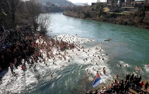 Choć Czarnogórców i Serbów wiążą bliskie więzi, w tym wyznanie, relacje obu narodów są bardziej powikłane niż w innych regionach dawnej Jugosławii. Na zdjęciu: kąpiąc się podczas prawosławnego Święta Jordanu w rzece Morača, płynącej przez stolicę Czarnogóry, jej mieszkańcy narodowości serbskiej demonstrują z flagą Serbii swoją odrębność. Podgorica, 19 stycznia 2026 r. // Fot. Stevo Vasiljevic / Reuters / Forum
