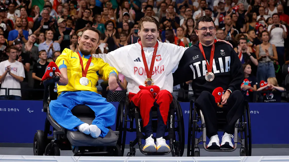 Kamil Otowski, zdobywca złotego medalu w pływaniu na 100 m stylem grzbietowym, na paraolimpiadzie w Paryżu. Obok srebrny medalista, Anton Kol (Ukraina), i brązowy, Francesco Bettella (Włochy), 29 sierpnia 2024 r. // Fot. Andrew Couldridge / Reuters / Forum
