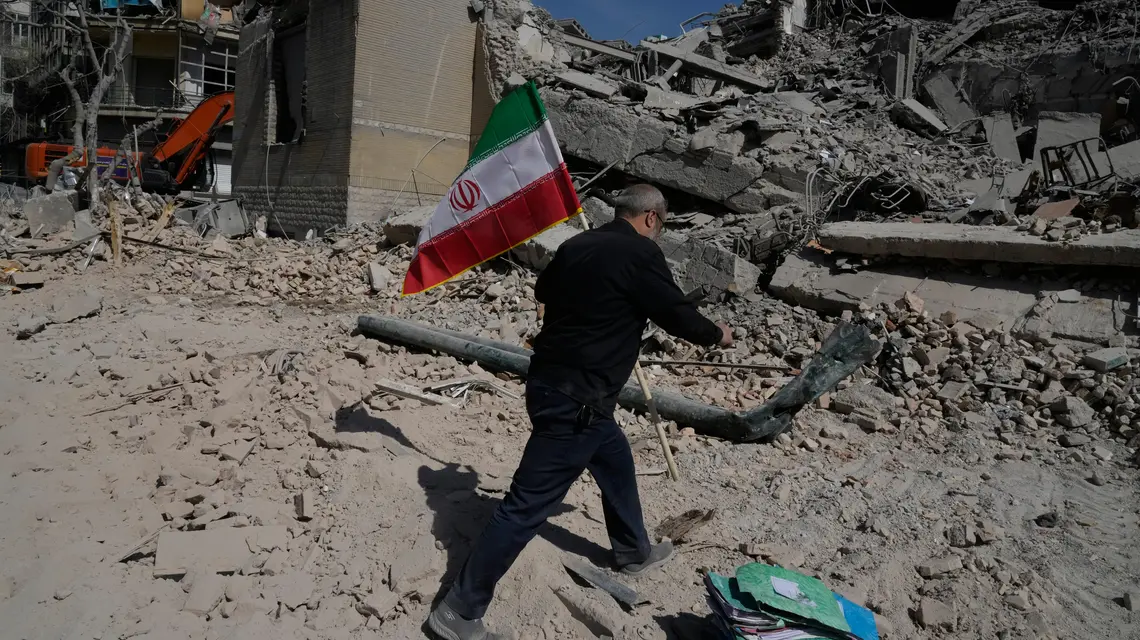 Mężczyzna niesie irańską flagę na gruzach budynków w Teheranie zbombardowanych podczas amerykańsko-izraelskiej kampanii wojskowej w Iranie, środa 4 marca 2026 r. / Vahid Salemi/Associated Press/East News