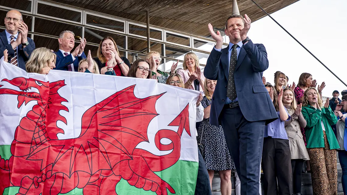 Rhun ap Iorwerth (z prawej), lider partii Plaid Cymru i nowy premier autonomicznego rządu Walii, wśród zwolenników z walijską flagą narodową. Czerwony smok na fladze pochodzi z legend arturiańskich, a biało-zielone barwy przyznano Walii za rządów dynastii Tudorów. Cardiff, 9 maja 2026 r. // Fot. Ben Birchall / PA / East News