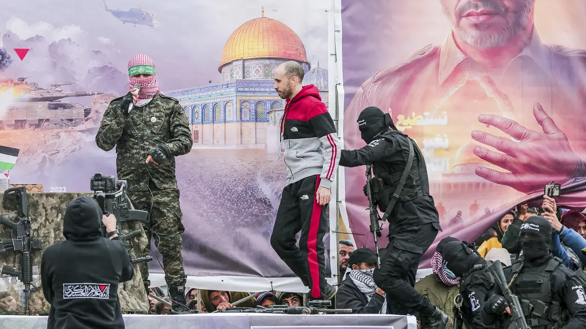 Zamaskowani bojownicy Hamasu pokazują tłumowi izraelskiego zakładnika przetrzymywanego od 7 października 2023 r., przed przekazaniem go Czerwonemu Krzyżowi. Rafah, Strefa Gazy, 22 lutego 2025 r. // Fot. Abood Abusalama / Middle East Images / AFP / East News