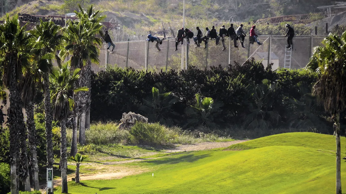 Migranci usiłują przejść przez zabezpieczenia na granicy Maroka z Melillą,  eksklawą Hiszpanii; po stronie „unijnej” – pole golfowe, 2014 r. / JOSE PALAZON / REUTERS / FORUM