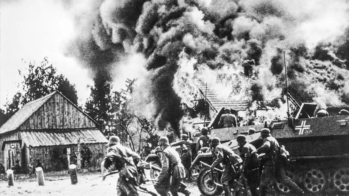 Niemieccy żołnierze w natarciu, w tle płonąca polska wioska. Wrzesień 1939 r. / BEW