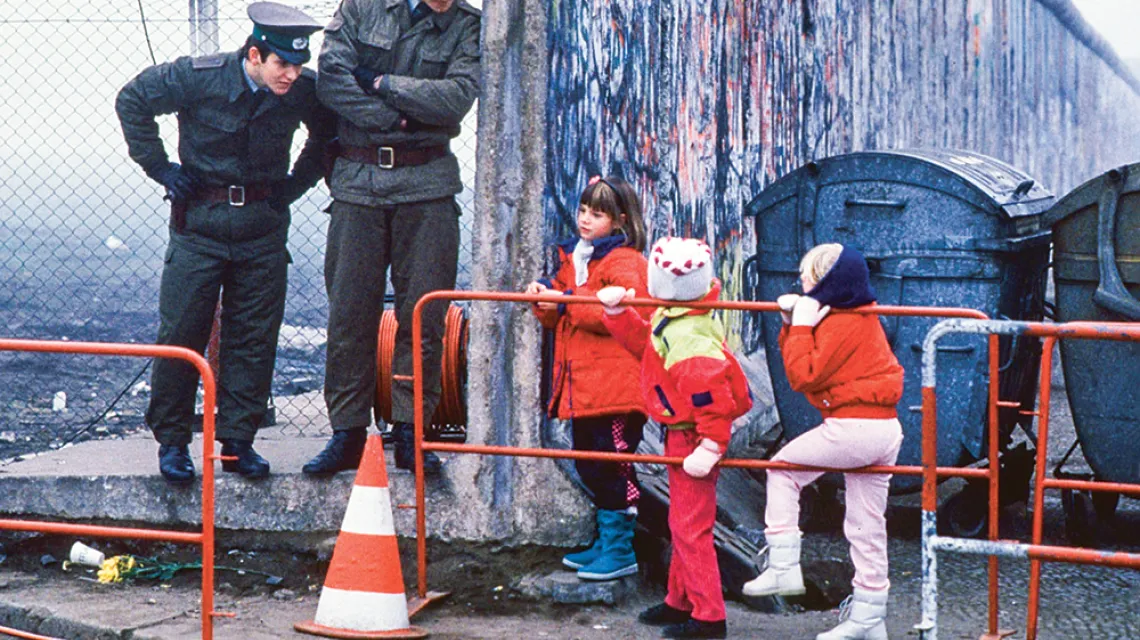 Dzieci z zachodnioniemieckich szkół i NRD-owscy strażnicy graniczni pięć dni po otwarciu muru berlińskiego, który przez 28 lat dzielił to miasto. Widoczny fragment muru. Berlin Wschodni, 14 listopada 1989 r.  / STEPHEN JAFFE / GETTY IMAGES