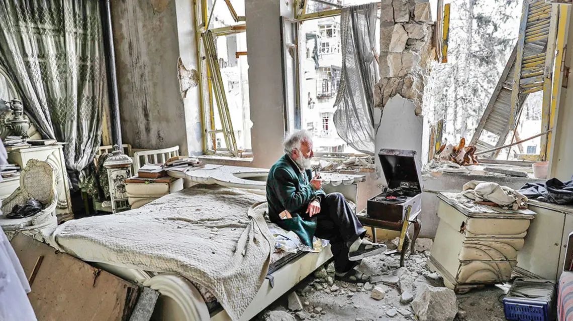 Abu Omar, 70-letni mieszkaniec syryjskiego Aleppo, słucha nagrań na gramofonie w swoim zniszczonym podczas walk domu, 2017 r. / JOSEPH EID / AFP / EAST NEWS