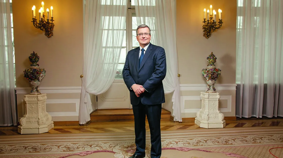 Zdjęcie przedstawia prezydenta Bronisława Komorowskiego stojącego w jednej z sal pałacu prezydenckiego.