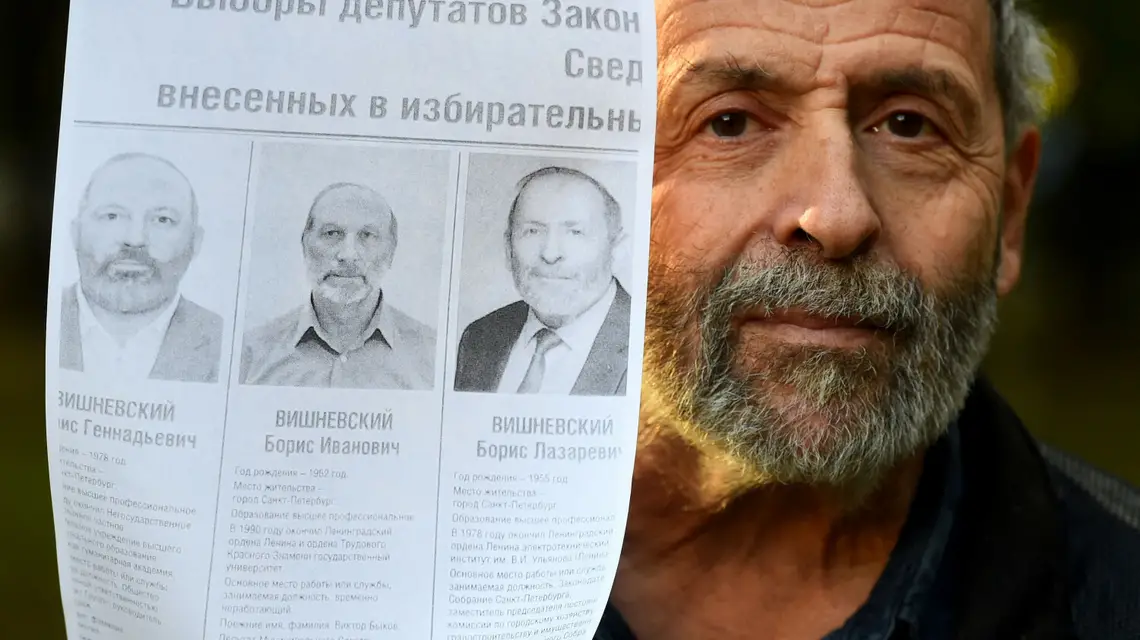 Borys Wiszniewski z opozycjnej partii Jabłoko trzyma plakat wyborczy, na którym występuje w otoczeniu dwójki "sobowtórów". OLGA MALTSEVA/AFP/East News / 
