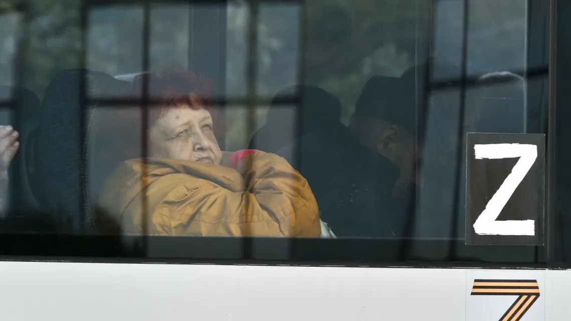 Kobieta ewakuowana z Chersonia wygląda przez okno autobusu udekorowanego symbolem rosyjskiej napaści na Ukrainę. Rosyjskie władze od kilku tygodni prowadzą ewakuację miasta. 2 listopada 2022 r. / fot. Associated Press/East News / 