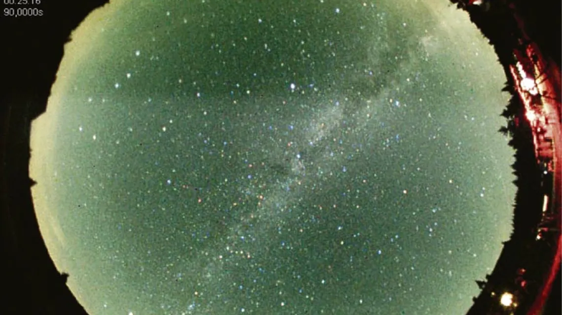 Dopiero w prawdziwych ciemnościach można podziwiać gwiazdy w całej krasie. Zdjęcie z szerokokątnej kamery obejmującej całe niebo. Po przekątnej biegnie Droga Mleczna. W prawym dolnym rogu budynek schroniska "Orle". Sierpień 2012 r.  / Fot. Sylwester Kołomański