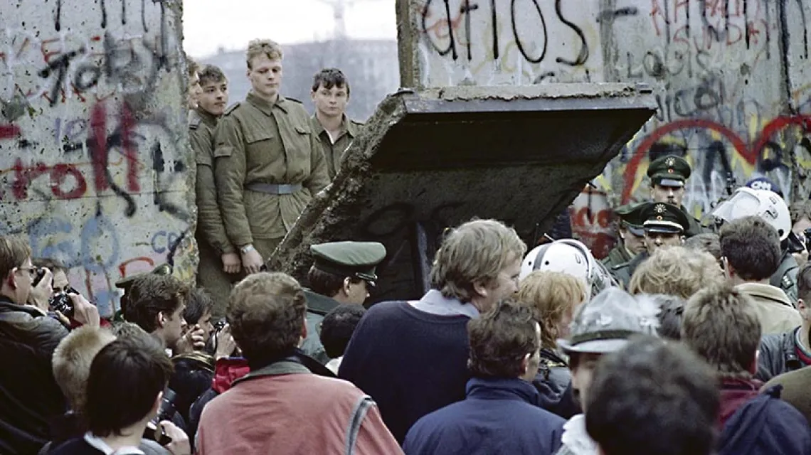 Mieszkańcy Berlina Zachodniego w pobliżu Potsdamer Platz obserwują żołnierzy straży granicznej z Berlina Wschodniego, wybijających przejście w murze. 11 listopada 1989 r. / Fot. Gerard Malie / AFP PHOTO / EAST NEWS