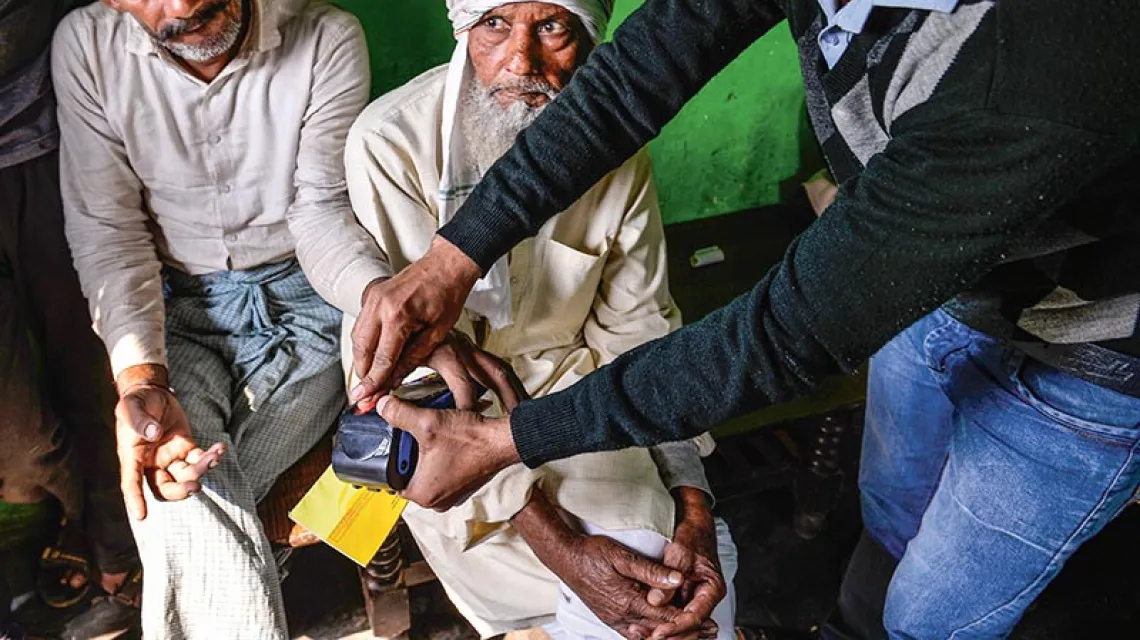 Pracownik banku pomaga autoryzować transakcję przy pomocy odcisków palców w jednej z wiosek stanu Uttar Pradeś na północy Indii, listopad 2016 r.  / Fot. Chandan Khanna / AFP / EAST NEWS
