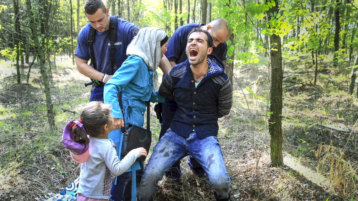 Węgierscy policjanci aresztują rodzinę syryjskich uchodźców, której udało się przedostać przez zasieki na granicy z Serbią, 28 sierpnia 2015 r. / / REUTERS / Bernadett Szabo