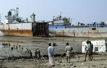 Robotnicy rozwijają przewód do palnika gazowego, którym będą wycinać metalowe części zezłomowanego statku. Chittagong, Bangladesz, grudzień 2004 r. // Fot. AMAN SHARMA / AP / East News