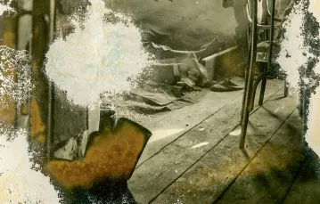 Album Piława Górna, 1.09.1939–31.10.1942. Izba w drewnianej wiejskiej chacie. Rozebrany do pasa mężczyzna w spodniach od munduru stoi plecami i ogląda się, prawdopodobnie w lustrze. Po lewej na podłodze widać nogi innych leżących żołnierzy. / / 