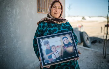 Fatma Senu trzyma w ręku kolaż, na którym są jej wnuki Alan i Galiba, a także córka Rihanna, Kobane, lipiec 2019 r. / PAWEŁ PIENIĄŻEK