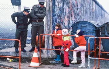 Dzieci z zachodnioniemieckich szkół i NRD-owscy strażnicy graniczni pięć dni po otwarciu muru berlińskiego, który przez 28 lat dzielił to miasto. Widoczny fragment muru. Berlin Wschodni, 14 listopada 1989 r. / STEPHEN JAFFE / GETTY IMAGES