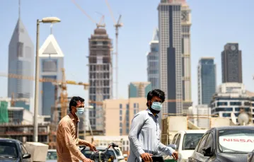 Imigranci pracujący w Dubaju pchają rowery przez dzielnicę Satwa / fot. KARIM SAHIB/AFP/East News / 