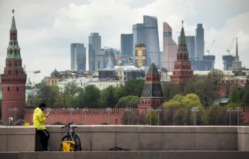 Kurier dostarczający jedzenie na moście w centrum Moskwy. W tle Kreml i budynki Moskiewskiego Międzynarodowego Centrum Biznesu, 6 maja 2020 r. / FOT. ALEXANDER NEMENOV/AFP/East News / 
