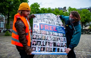 Para trzyma plakat z portretami więźniów politycznych w Rosji i na Białorusi podczas protestu w Hadze. 20 maja 2021 r. /Nur Photo/East News / 