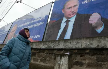 Mieszkanka Krymu przechodzi obok plakatów na których widnieją napisy: „Rosja nie zaczyna wojen, ona je kończy” i „Będziemy dążyć do demilitaryzacji i denazyfikacji Ukrainy”. Centrum Symferopola, 4 marca 2022 r. / STRINGER/AFP/East News / 