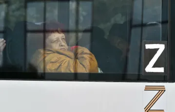 Kobieta ewakuowana z Chersonia wygląda przez okno autobusu udekorowanego symbolem rosyjskiej napaści na Ukrainę. Rosyjskie władze od kilku tygodni prowadzą ewakuację miasta. 2 listopada 2022 r. / fot. Associated Press/East News / 