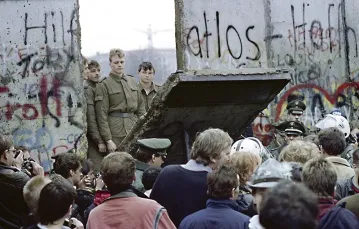 Mieszkańcy Berlina Zachodniego w pobliżu Potsdamer Platz obserwują żołnierzy straży granicznej z Berlina Wschodniego, wybijających przejście w murze. 11 listopada 1989 r. / Fot. Gerard Malie / AFP PHOTO / EAST NEWS