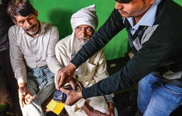 Pracownik banku pomaga autoryzować transakcję przy pomocy odcisków palców w jednej z wiosek stanu Uttar Pradeś na północy Indii, listopad 2016 r. / Fot. Chandan Khanna / AFP / EAST NEWS