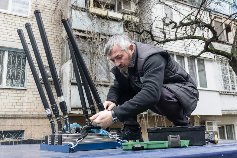 Maks na dachu opancerzonego auta naprawia anteny mobilnej zagłuszarki – niezbędnego wyposażenia samochodów poruszających się w strefie nad rzeką, gdzie gęsto od dronów. Chersoń, 4 grudnia 2024 r. // Fot. Antonina Palarczyk